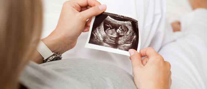 Eine schwangere Frau betrachtet das Ultraschallbild ihres ungeborenen Kindes (© shutterstock)